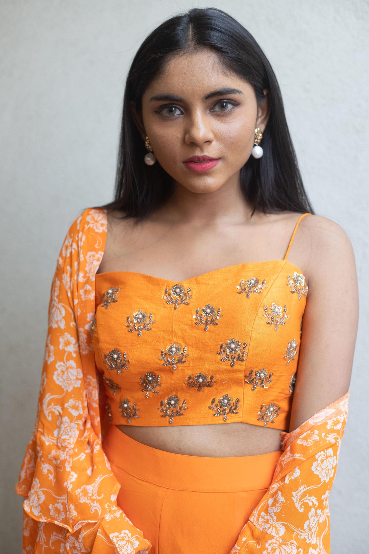 Hand embroidered orange blouse with a high waisted straight pant and floral ruffle cape